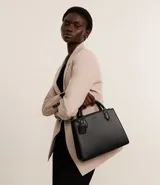 Cartera satchel negra de material sintético con textura diagonal, doble asa de mano y asa larga removible de gross. Incluye porta monedas y cierre por cremallera.