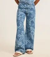Pantalón femenino de jeans, modelo wide leg, color celeste desgastado con estampado floral en tono más claro. Presenta trabillas en la cintura, cierre tradicional y pespuntes contrastantes.