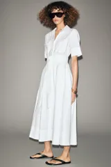 Vestido midi camisero color ladrillo, confeccionado en popelina de algodón. Presenta cuello solapa, manga corta con puños abotonados, bolsillos laterales ocultos y bolsillos de parche con solapa en el pecho. Incluye cinturón lazada en el mismo tejido y cierre frontal con botones ocultos.