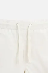 Bañador corto color blanco hueso de tejido técnico, con cintura elástica ajustable con cordón, bolsillos laterales y trasero.