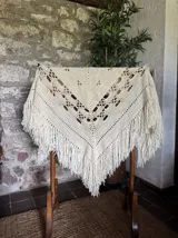Ruana color crema tejida a crochet con diseño calado y flecos largos.