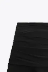 Falda pantalón corta de color negro, con tiro medio, detalle de pliegues en la cintura y volantes en el ruedo. Cierre lateral con cremallera.