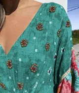 Túnica corta verde con estampado de flores rojas y detalles bordados. Mangas anchas con terminación en volados con estampado floral en tonos rosa y celeste.