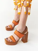 Sandalias de plataforma color naranja con detalles en marrón. Tienen tiras anchas sobre el empeine y el tobillo, y un tacón cuadrado alto.