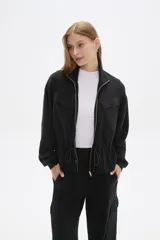 Campera negra de poliéster con cierre frontal, cuello alto, bolsillos con solapa en el pecho y cintura ajustable con cordón.