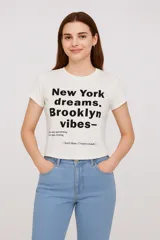 Remera blanca de algodón con cuello redondo y mangas cortas. Estampado frontal con la frase "New York dreams, Brooklyn vibes" en letras negras.