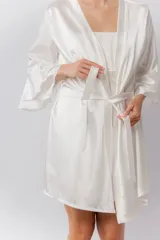Bata blanca de satén elastizado, con mangas tres cuartos con volados y largo por encima de la rodilla. Incluye lazo para ajustar en la cintura.