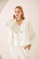 Camisa oversize blanca de lino, con cuello en V, mangas largas abullonadas con puños elásticos y lazos decorativos.