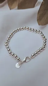 Pulsera de esferas plateadas de 5mm de diámetro, con cierre de mosquetón y dije redondo con el sello "S925".