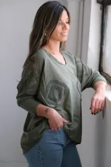 Remera verde militar con cuello en V y mangas 3/4. Presenta apliques circulares con textura en el frente y los hombros.