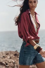 Shorts de denim blanco, tiro alto, estilo mom fit, con cinco bolsillos y cierre frontal con cremallera y botón.