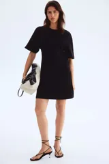 Vestido corto negro de punto de algodón suave con cuello redondo ribeteado acanalado, hombros caídos y mangas al codo. Pinzas moldeadoras en la parte posterior de la cintura para estilizar la figura.