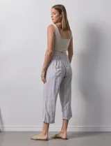 Pantalón capri de lino a rayas verticales en tonos grisáceos y beige, con cintura elástica y lazo ajustable.
