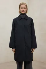 Chaqueta negra de largo medio, con cuello camisero y cierre frontal de botones. Presenta un corte holgado y mangas anchas.