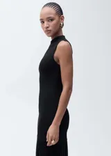 Vestido negro de punto ajustado al cuerpo, sin mangas y con cuello alto. Largo hasta la rodilla y ruedo con flecos.