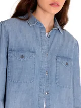 Camisa de manga larga celeste de denim con dos bolsillos en el pecho y cierre con botones metálicos.