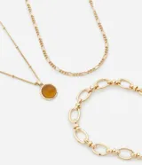 Set de tres collares dorados de diferentes largos y diseños. Incluye un collar con colgante circular de resina color ámbar, un collar de cadena fina y un collar de cadena gruesa con eslabones ovalados.