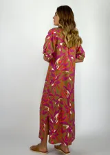 Vestido largo tipo camisero con estampado floral en tonos fucsia, blanco y naranja sobre fondo verde oliva.
