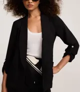 Blazer negro confeccionado en tejido airflow, con solapa en el cuello y abertura total. La prenda tiene martingalas en los puños, que son tiras con botones.