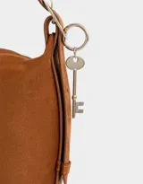 Bandolera color marrón camel de cuerina con textura gamuzada, asa corta de hombro y charm lateral.