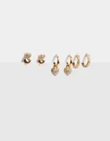 Set de tres pares de aros dorados: un par de aros tipo botón con forma de corazón, un par de aros tipo argolla con dije de corazón con strass y un par de aros tipo argolla con strass.