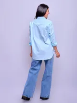 Camisa blanca de algodón, corte holgado, con cuello clásico y botones frontales. Las mangas son largas y se ven remangadas.