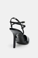 Zapato de tacón destalonado color negro charol, con punta fina, tacón fino alto y tiras finas con hebillas ajustables al tobillo.
