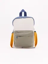 Mochila pequeña de colores, ideal para niños en edad preescolar. Cuerpo principal color crema, con borde superior y asa de agarre en azul oscuro. Bolsillo frontal grande en color verde oliva y bolsillos laterales en color mostaza/naranja.