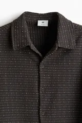 Camisa marrón con textura de punto, cuello inglés, tapeta lisa y mangas largas con puños abotonados.