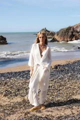 Túnica blanca de lino, con mangas anchas y cuello en V profundo. La prenda se ata a la cintura con un lazo del mismo tejido.