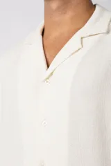 Camisa de manga corta color crudo, confeccionada en lino texturizado. Tiene cuello tipo cubano, cierre frontal con botones y corte recto.