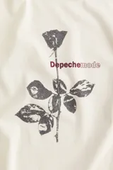 Remera color crema de corte amplio con estampado de una rosa y el nombre de la banda Depeche Mode en color rojo.