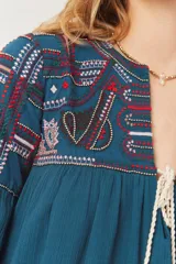 Vestido azul petróleo con bordados en el canesú y mangas, escote en V con cordones y mangas largas abullonadas.