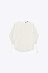 Blusa blanca de lyocell con cuello redondo, manga corta abullonada ajustable con cordones, bajo redondeado y cierre en la espalda con abertura y botón.