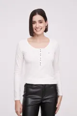 Remera de manga larga entallada en color blanco, confeccionada en algodón. Presenta cuello redondo con una hilera de botones frontales y un pequeño bolsillo en el pecho con detalle de botón.