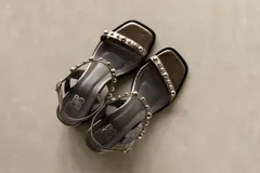 Sandalia de cuero color marrón con taco bloque medio y punta cuadrada. Presenta tachas esféricas doradas en las tiras y hebilla de ajuste en el tobillo.