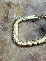 Pulsera dorada con eslabones tipo espiga y cierre de mosquetón.