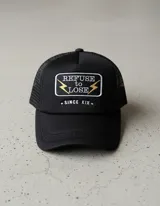 Gorra trucker negra con parche bordado con el texto "Refuse to Lose" y dos rayos dorados.
