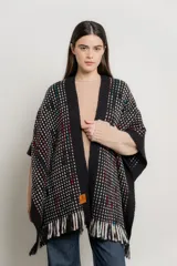 Ruana tejida color negro con diseño geométrico en blanco, celeste y rojo. Presenta cuello abierto y flecos en el ruedo.