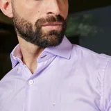 Camisa de hombre de algodón, color celeste con rayas verticales blancas finas. Tiene cuello clásico, manga larga con puños abotonados y un pequeño logo bordado en el pecho.