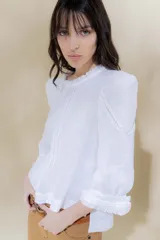 Blusa de lino blanca con escote a la base y terminación de voladito al bies desflecado. Delantera con alforzas verticales y mangas románticas tres cuartos, con detalle de puntilla. Puños con alforzas y voladitos que suman un toque femenino. Espalda abotonada.