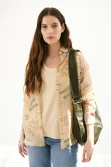 Camisa beige de manga larga con cuello clásico y cierre frontal con botones. Presenta bordados con motivos florales y geométricos en tonos azules, rojos y verdes.