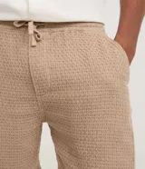 Bermuda de hombre color blanco crudo, confeccionada en algodón texturizado. Presenta un corte comfort, cintura elástica con lazo ajustable y bolsillos laterales.