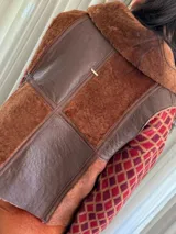 Chaleco marrón con cierre frontal, cuello de piel sintética y diseño patchwork con bloques de cuero y piel sintética.