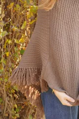 Poncho tejido en lana merino color marrón topo, con cuello redondo y terminación con flecos.