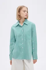 Camisa a rayas verticales verdes y blancas, de corte holgado, manga larga con puños abotonados, cuello clásico y bolsillo de parche en el pecho.