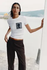 Camiseta blanca de algodón con cuello redondo y mangas cortas. Presenta un bolsillo de tul con una flor bordada y abalorios en el delantero.