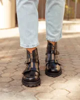 Botas de cuero negras con suela track, cierre frontal dorado y dos hebillas decorativas en el empeine.