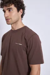 Remera de manga corta color marrón oscuro con cuello redondo y un pequeño texto bordado en blanco en el pecho.
