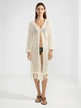 Cárdigan largo de algodón color crudo, tejido con punto abierto y detalles de flecos en el ruedo.